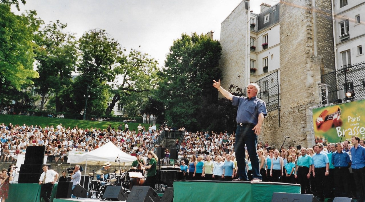 Jean-Claude Valembois dirigeant un grand chœur en plein air