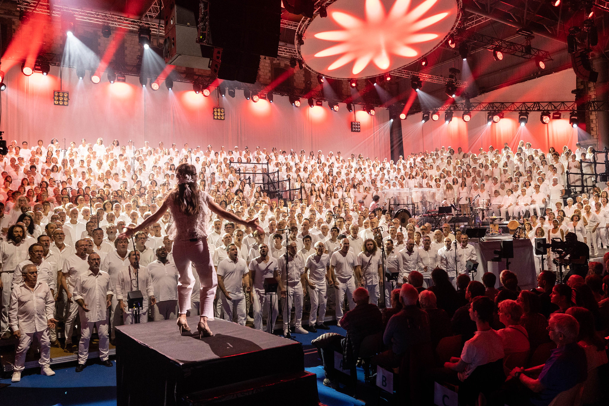 Le Grand Choral face à la cheffe de chœur dans une lumière rouge